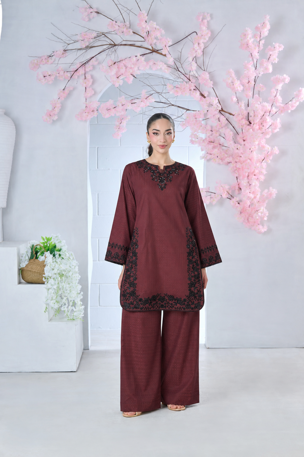 Woman wearing a maroon embroidered fabric tunic and matching wide-leg trousers in front of pink blossoms.