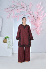 Woman wearing a maroon embroidered fabric tunic and matching wide-leg trousers in front of pink blossoms.