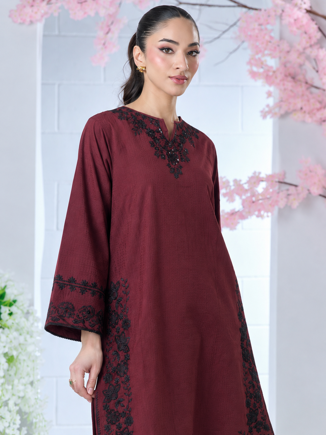 Maroon fabric tunic with black floral embroidery on the neckline, sleeves, and sides, worn by a woman.